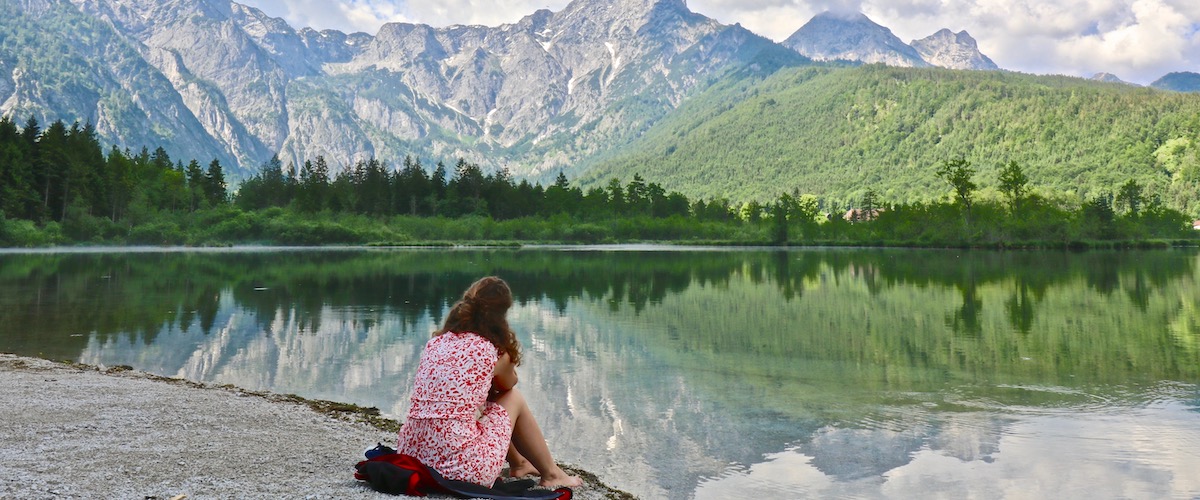 Eine junge Frau sitzt am Ufer des Almsees mit den Bergen im Hintergrund