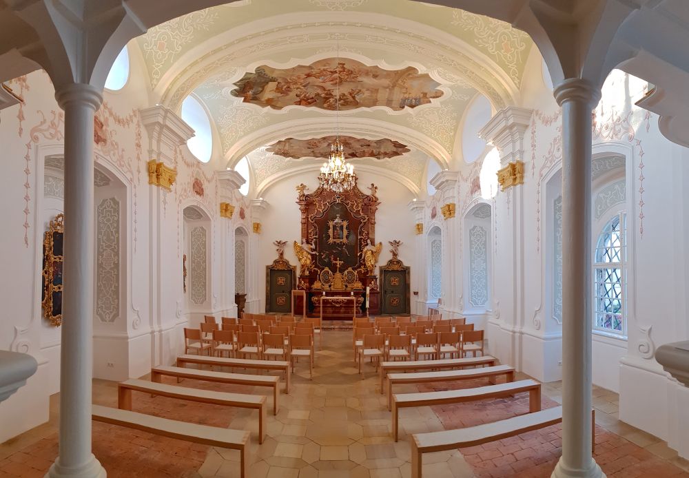 Innenraum der akademischen Kapelle, mit deren schlichten weißen Wänden, den sauber restaurierten Wandmalereien und der hellen Holzbestuhlung